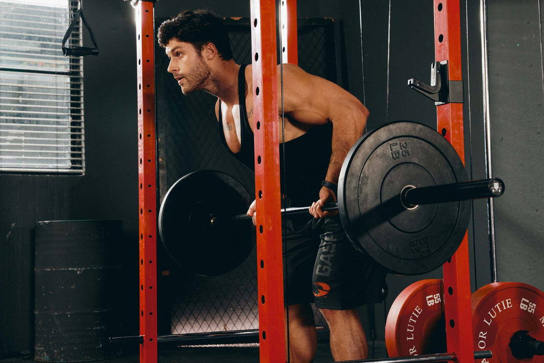 A man performing a barbell row exercise using a power rack in a home gym.