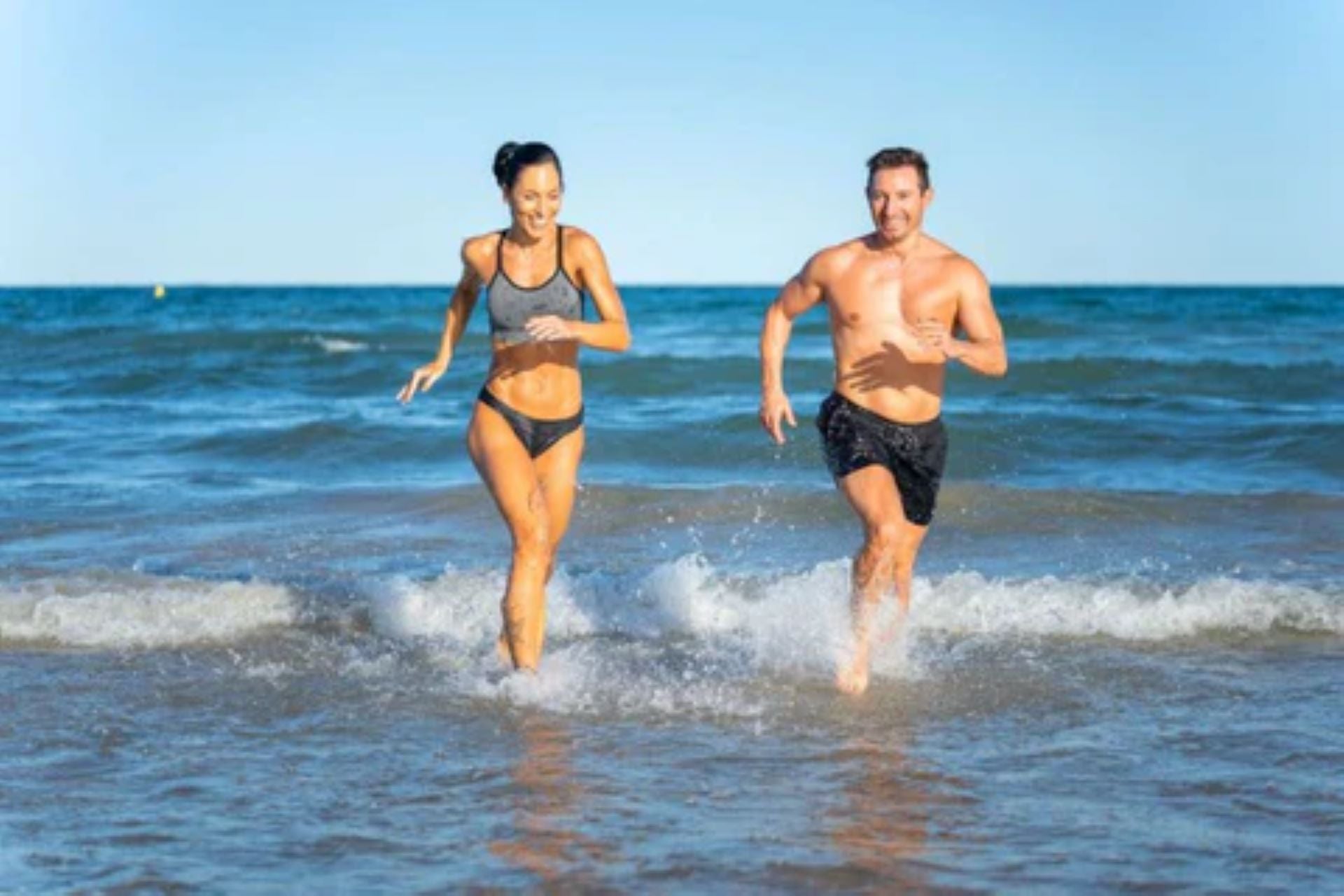 Man and woman engaging in cardio training by running along the beach for outdoor fitness.