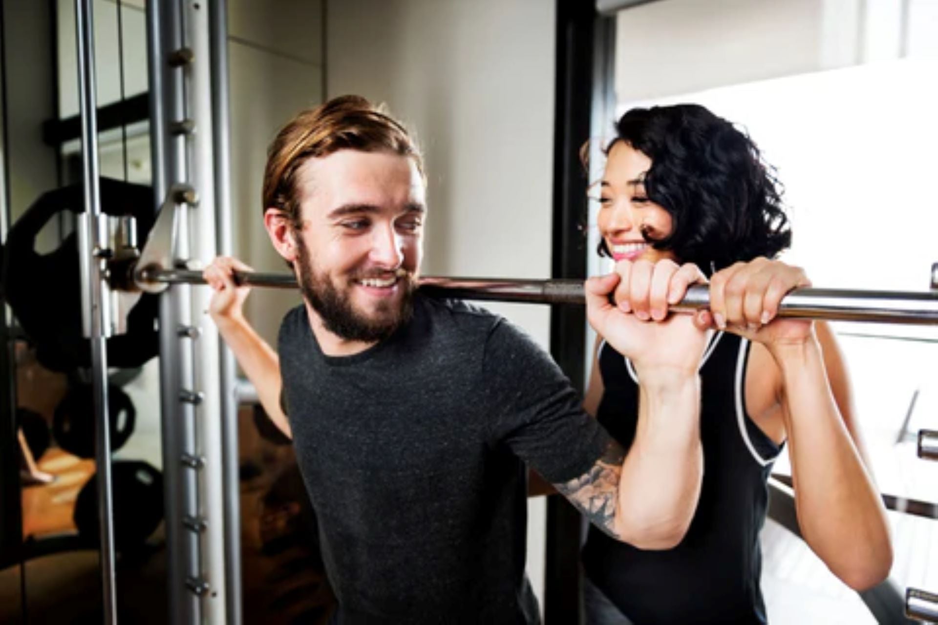 Man and woman doing a weightlifting exercise together in a home gym setting.