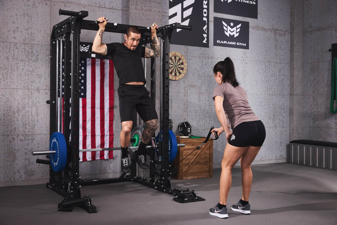 Two individuals doing pull-ups and cable exercises on a smith machine in a gym setting.