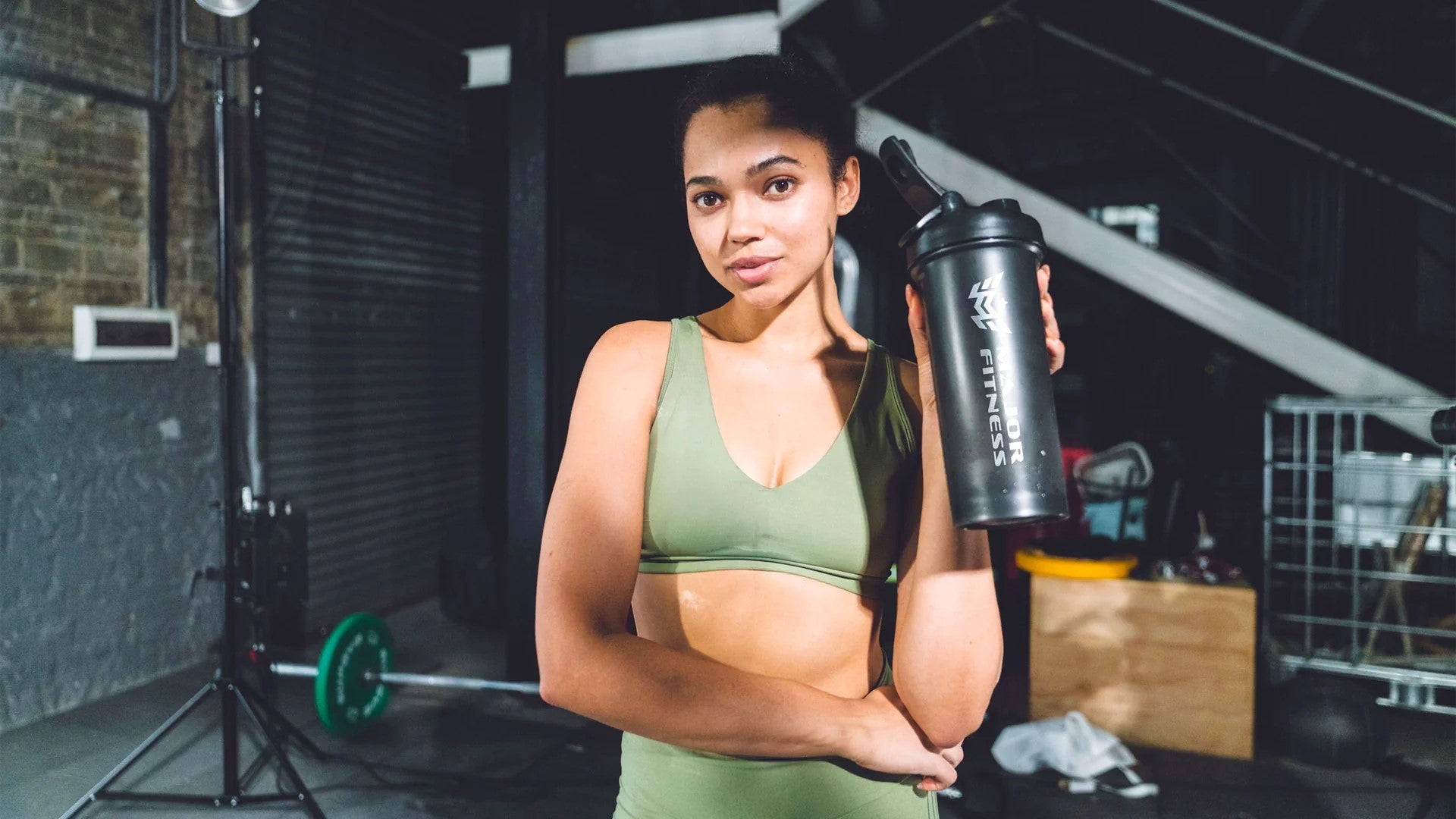 Female athlete hydrating with a recovery drink in the gym, emphasizing post-exercise recovery.