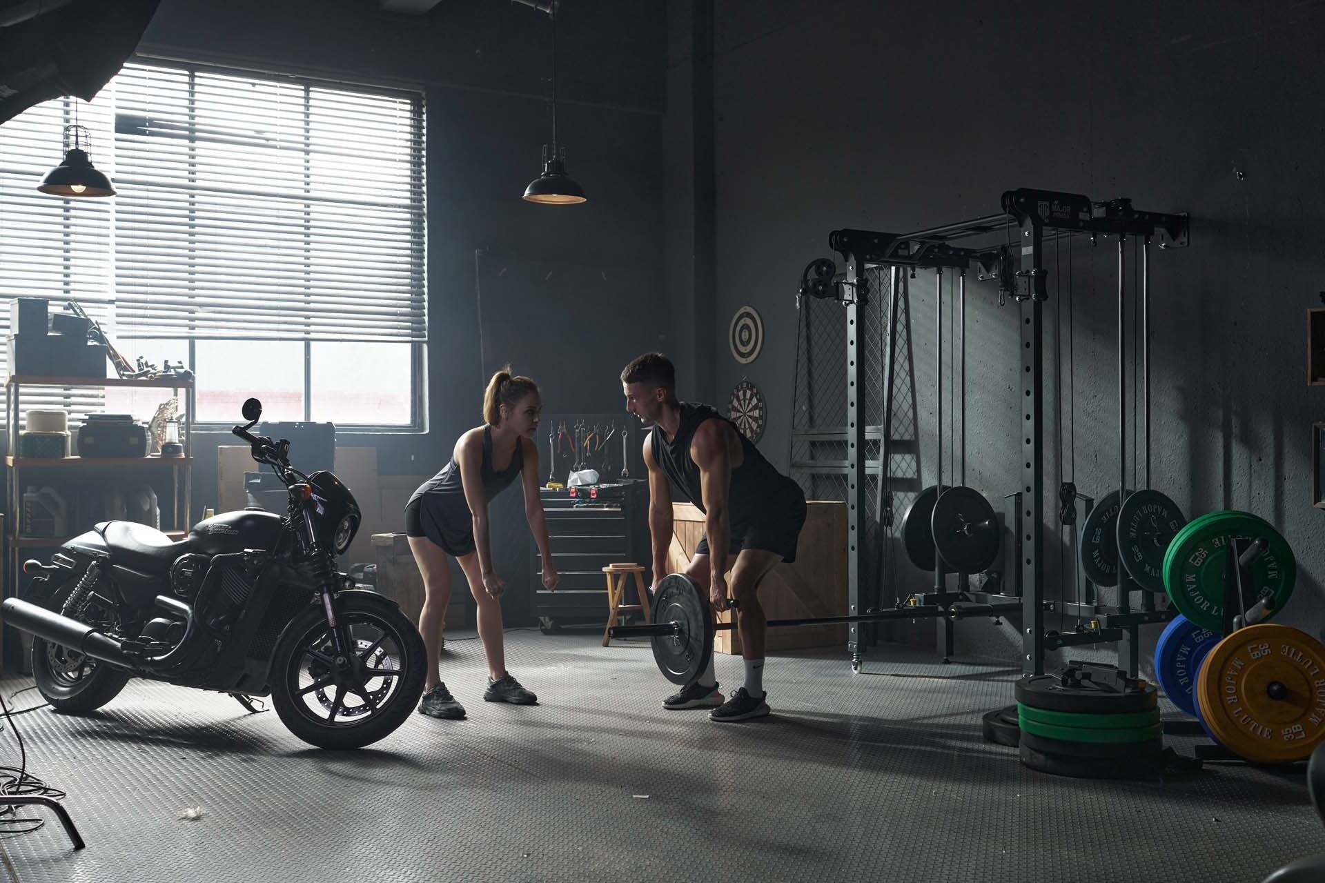  Couple doing deadlift exercises with a Smith machine in a well-equipped home gym.