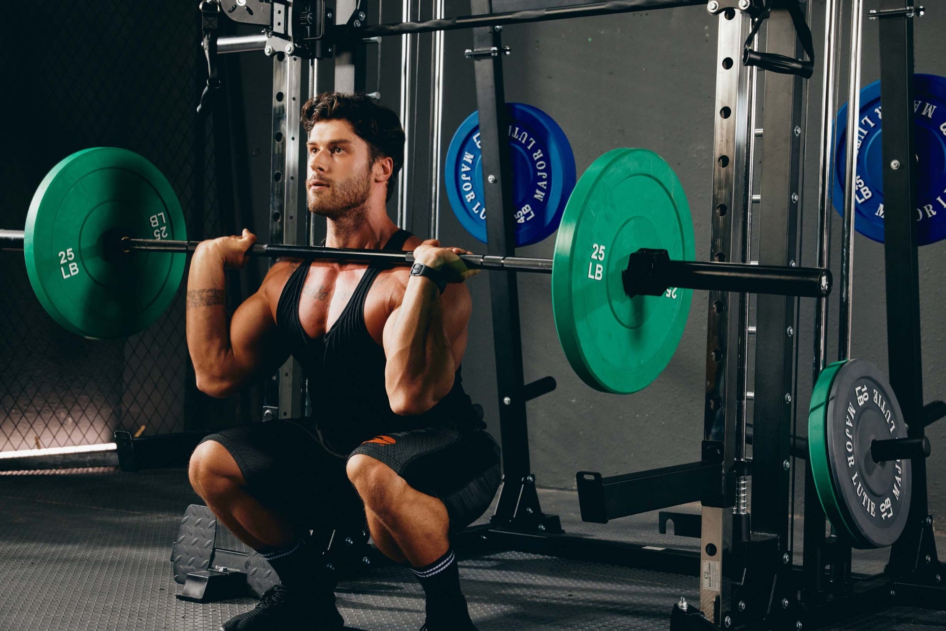 A man engaged in a front squat workout on a Smith machine with weight plates, in a home gym environment.