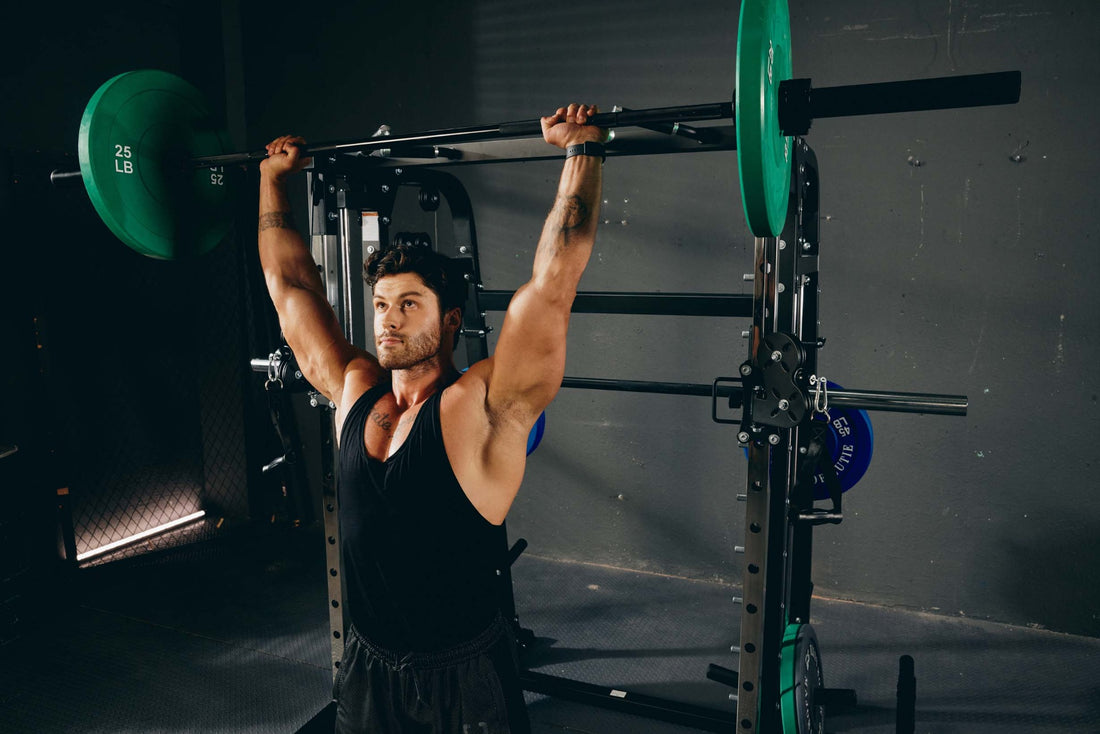 Man performing overhead press with a barbell on a Smith machine in a home gym.