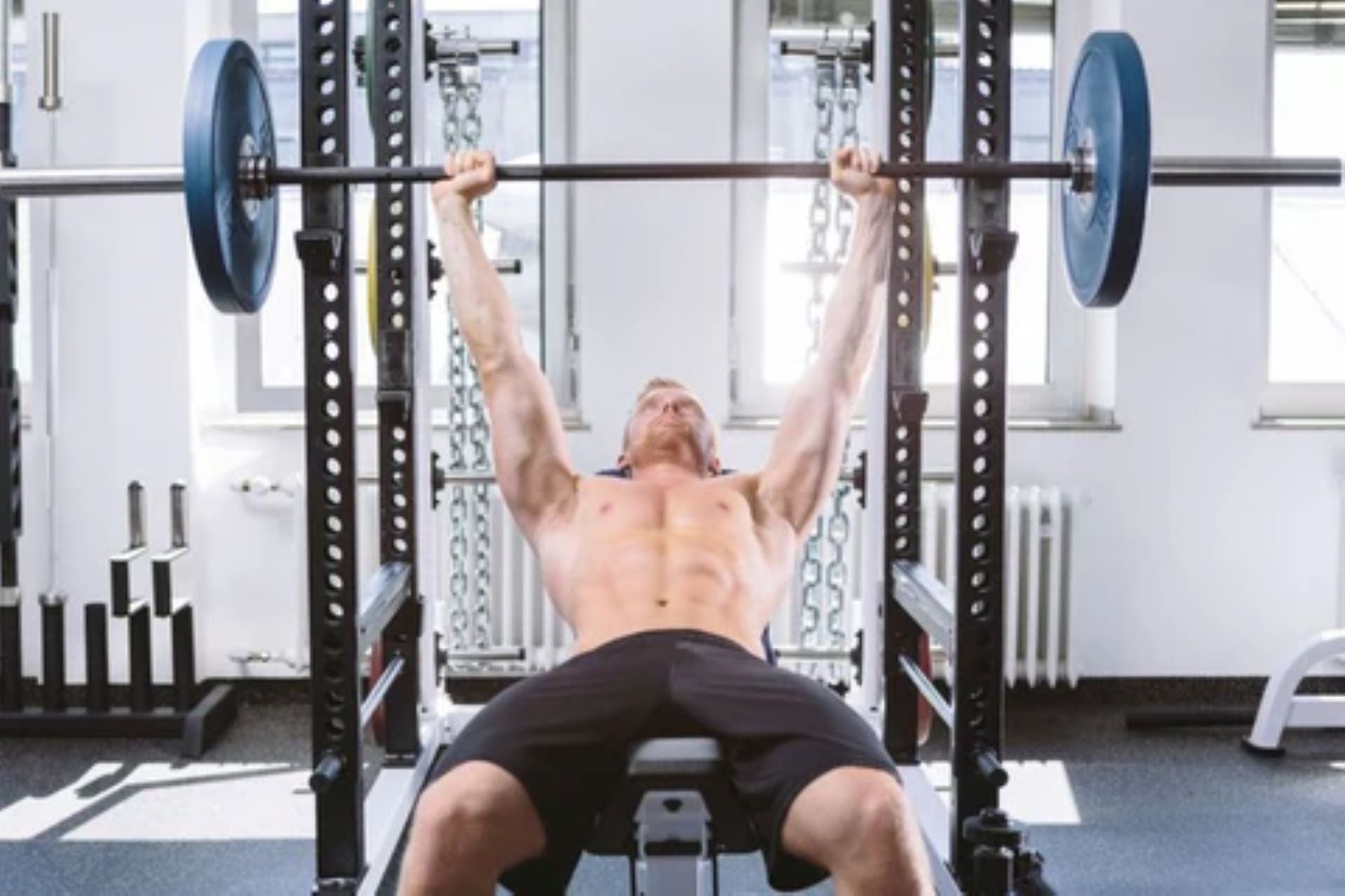 Man performing a bench press using a power rack in a home gym.