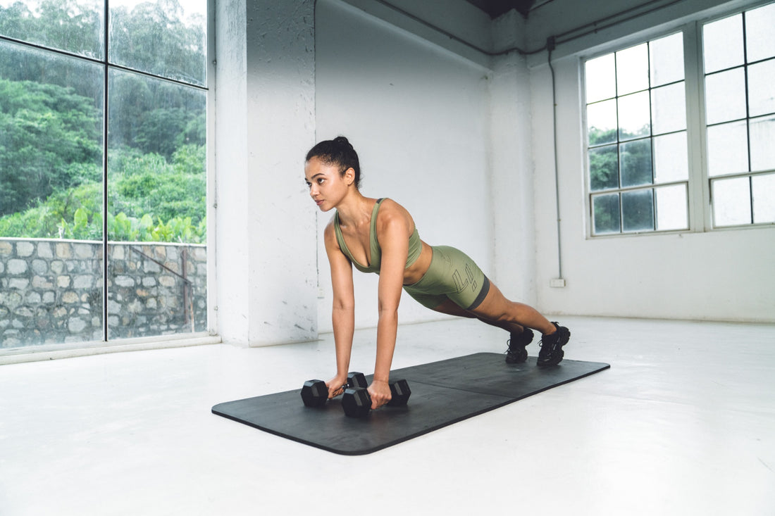 Woman doing a plank exercise with dumbbells in a home workout setting.