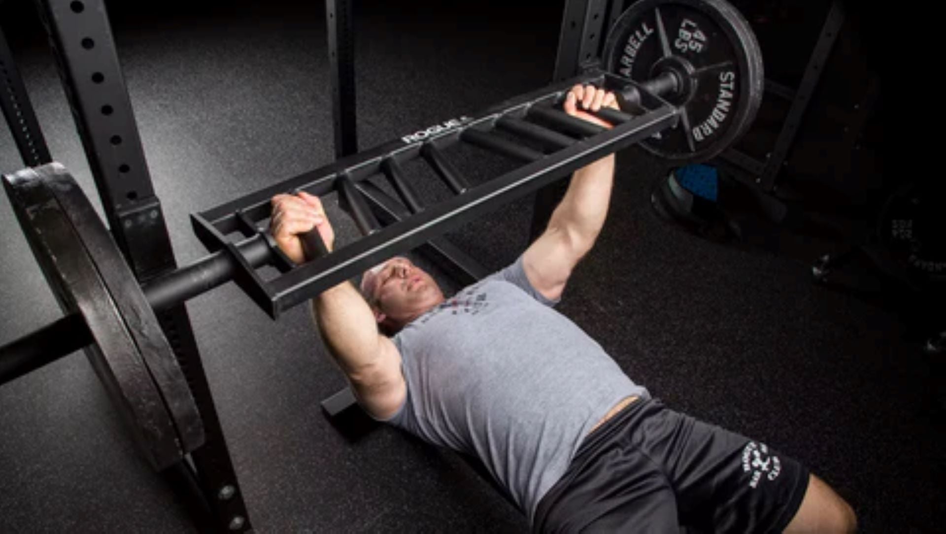 man performing bench press with specialty barbell in home gym setup