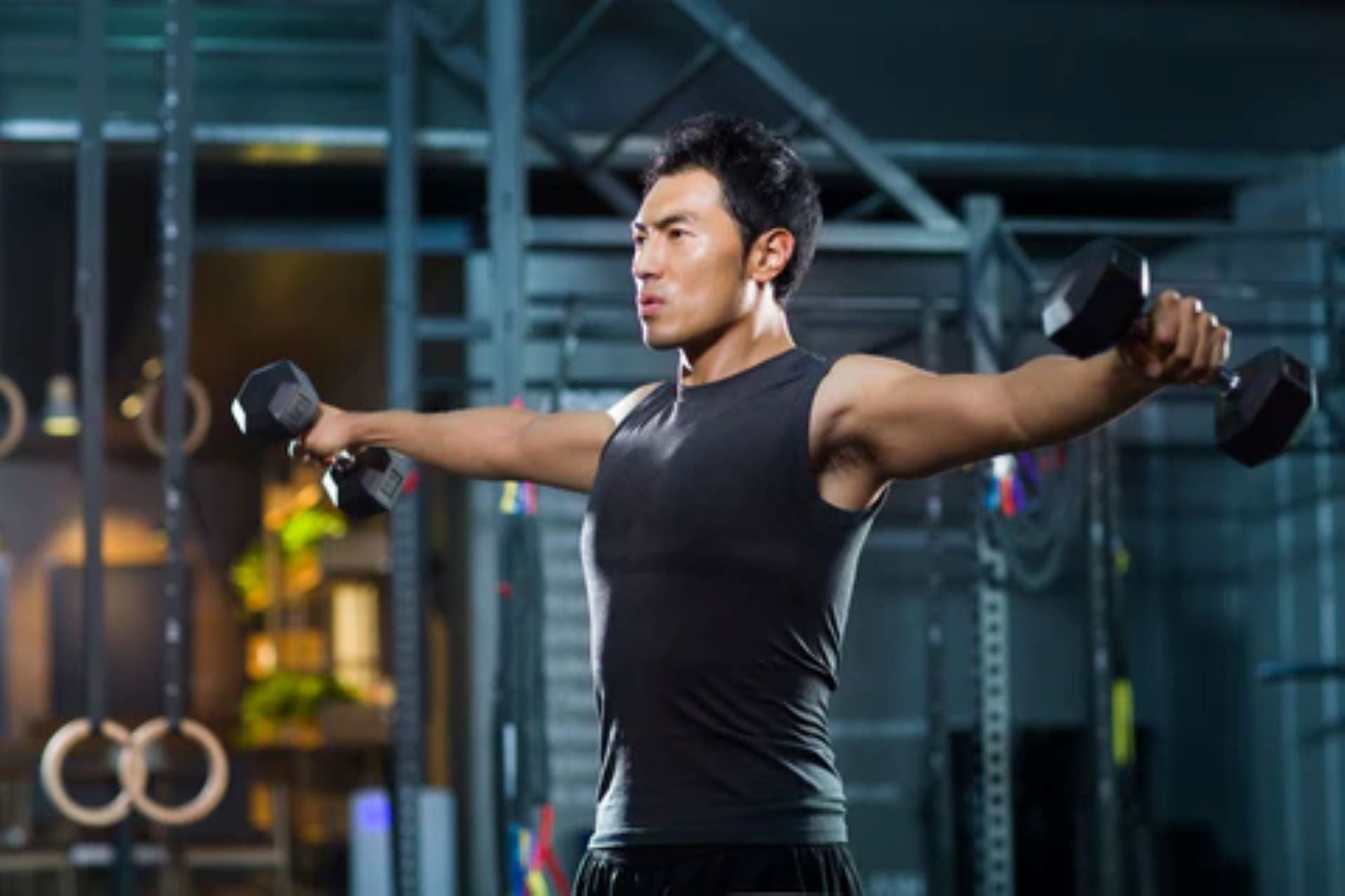 Man performing a dumbbell lateral raise exercise in a gym.