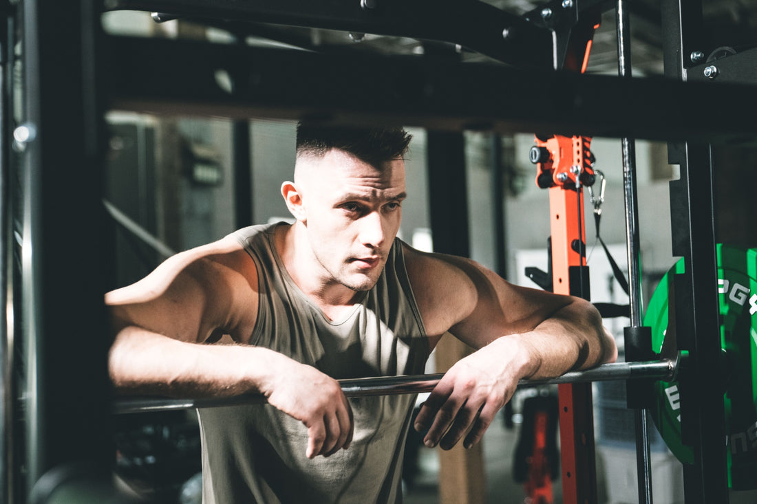 Man leaning on a Smith machine barbell for rest after exercise.