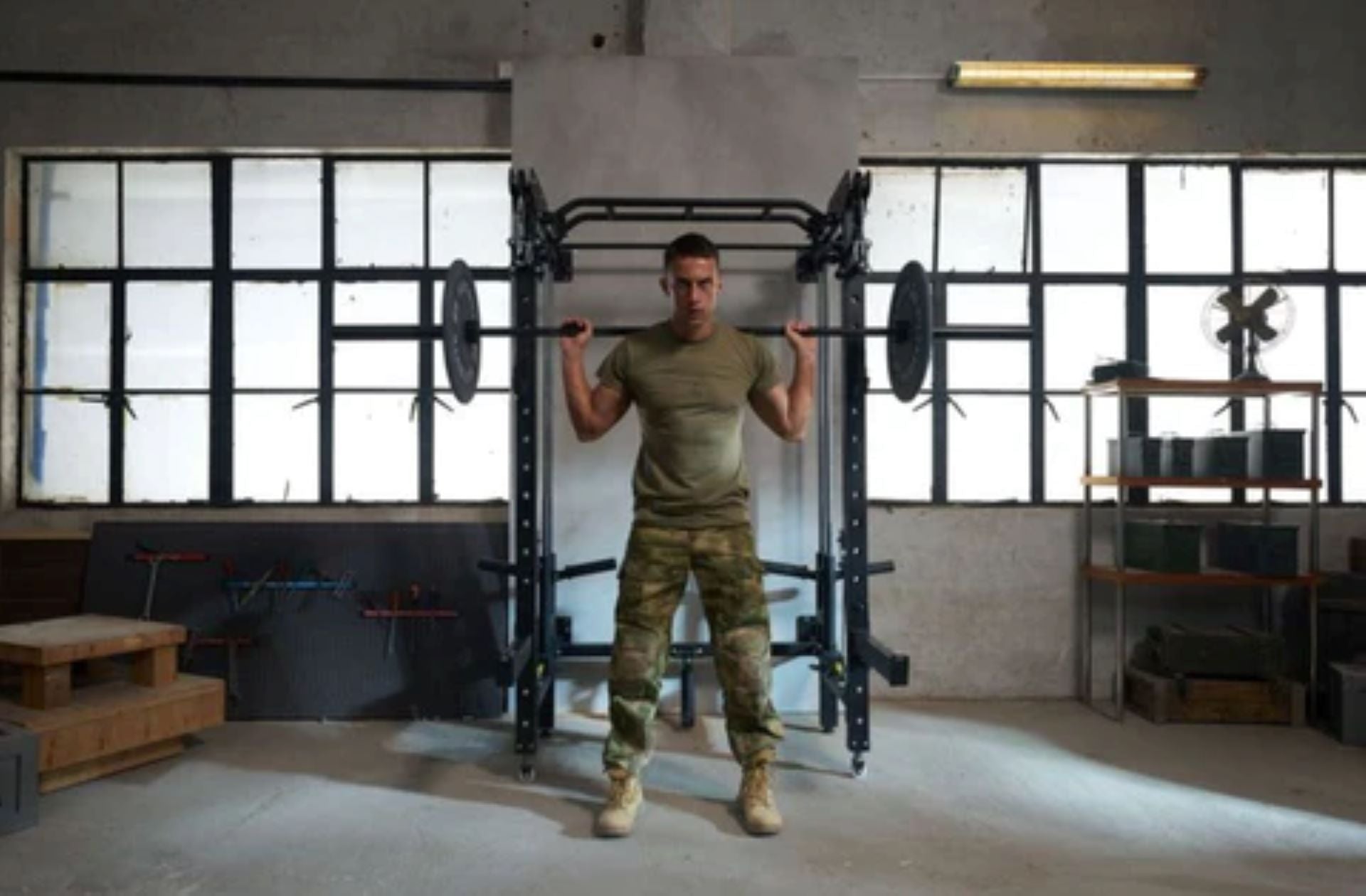 Man in camouflage pants performing a barbell squat in a military training environment.