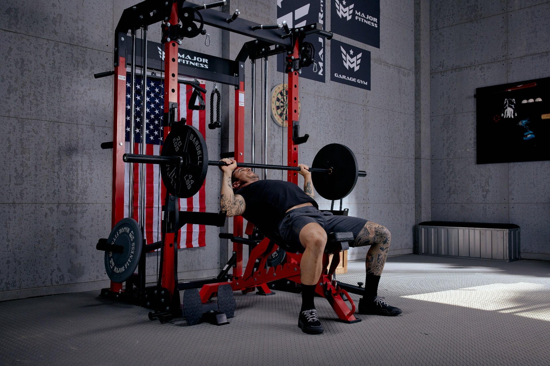 Man lifting a barbell on a bench press in a home gym equipped with a power rack and barbell plates.