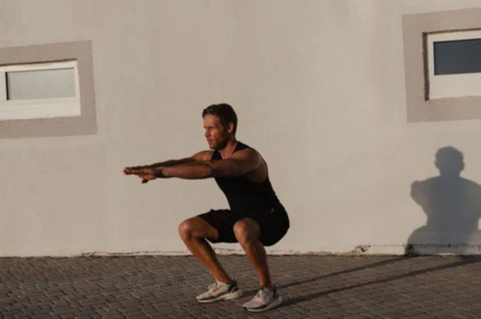 Man performing a bodyweight squat exercise outdoors against a wall.