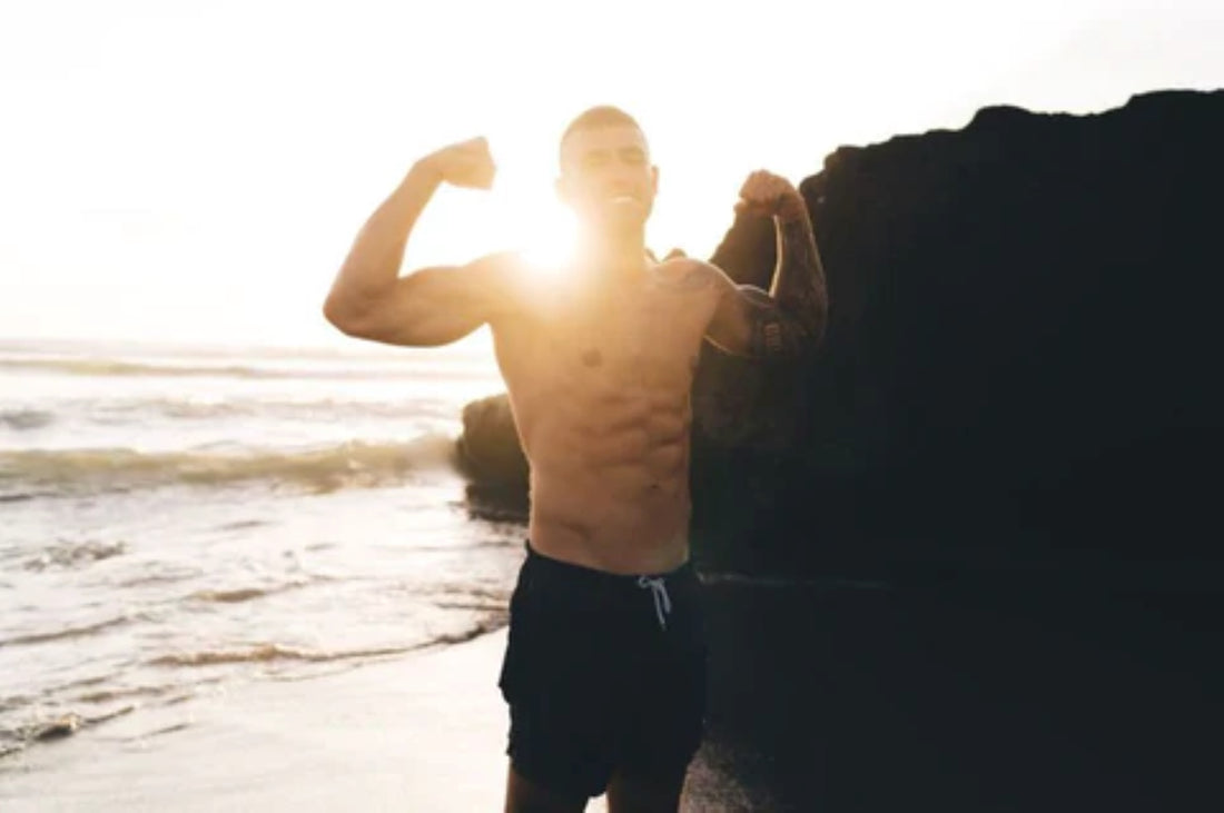 Man flexing muscles outdoors with sunlight highlighting his physique, representing fitness and strength.