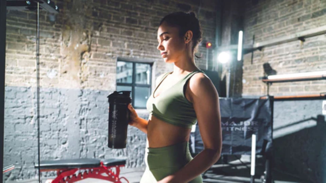 Woman in green sportswear holding a protein shake after a workout in a home gym.