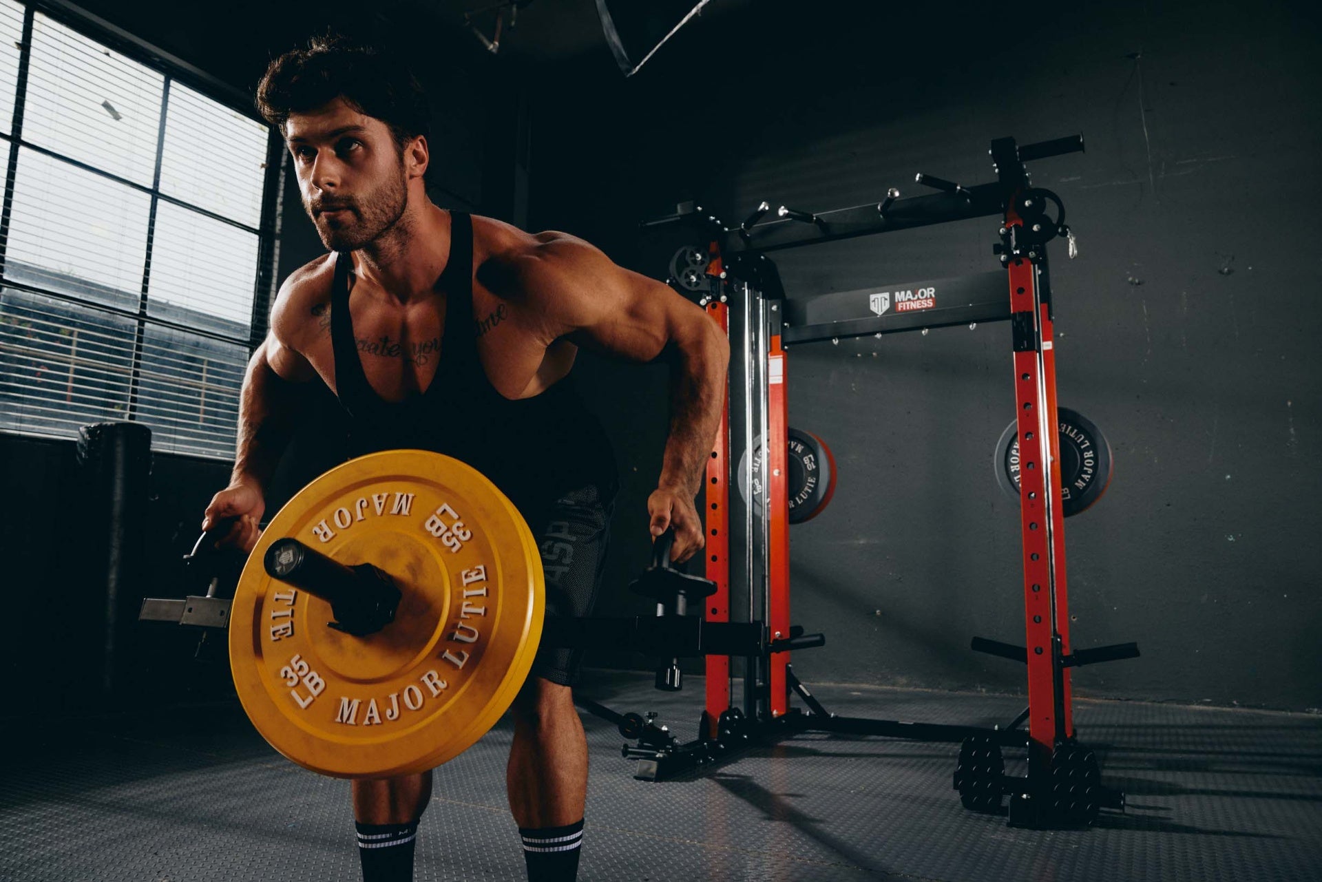 Man performing a barbell row exercise with yellow plates on a power rack.