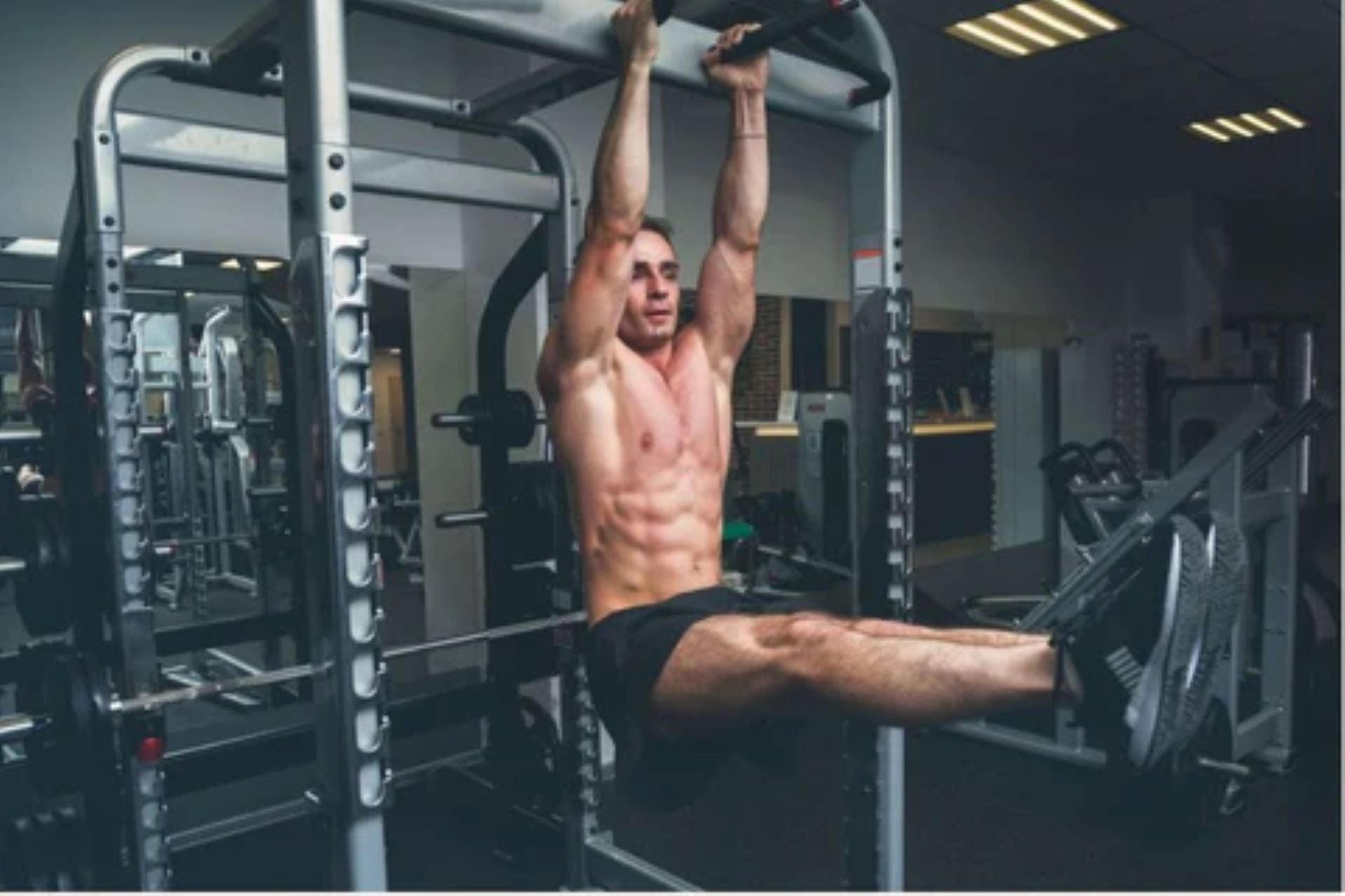 man performing pull-up with hanging leg raise on Smith machine for core and upper body strength.