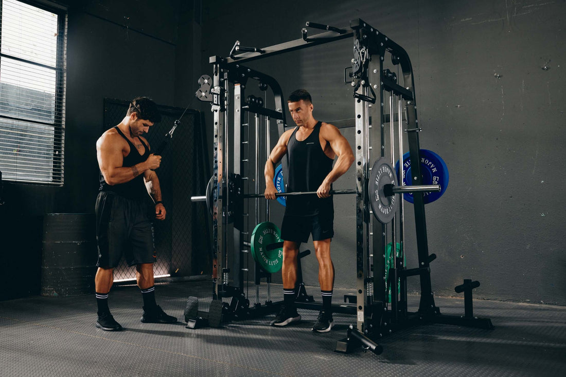 Two men performing a strength training workout using a Smith machine in a gym.