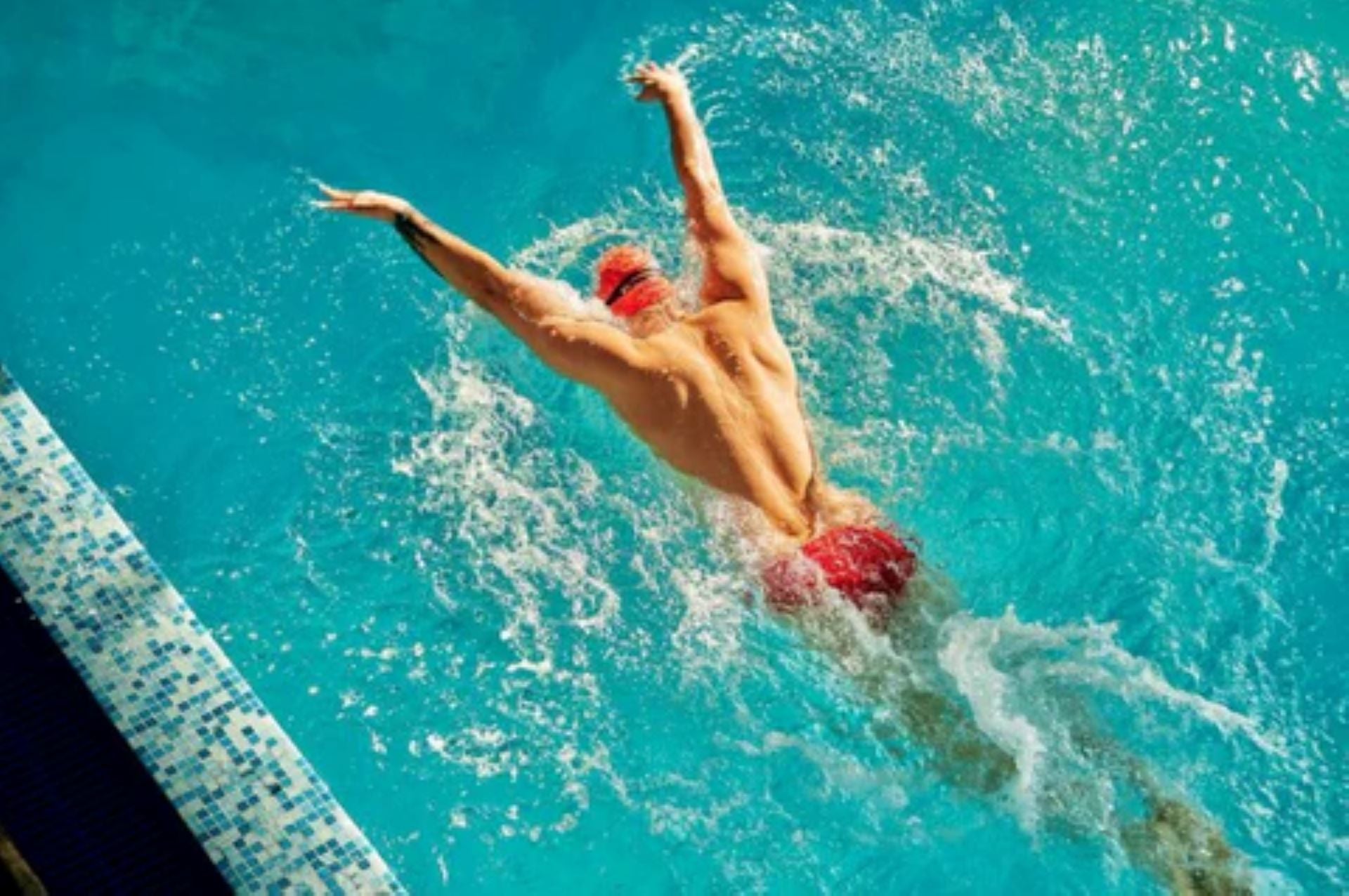 A swimmer performing the butterfly stroke in a pool, viewed from above.