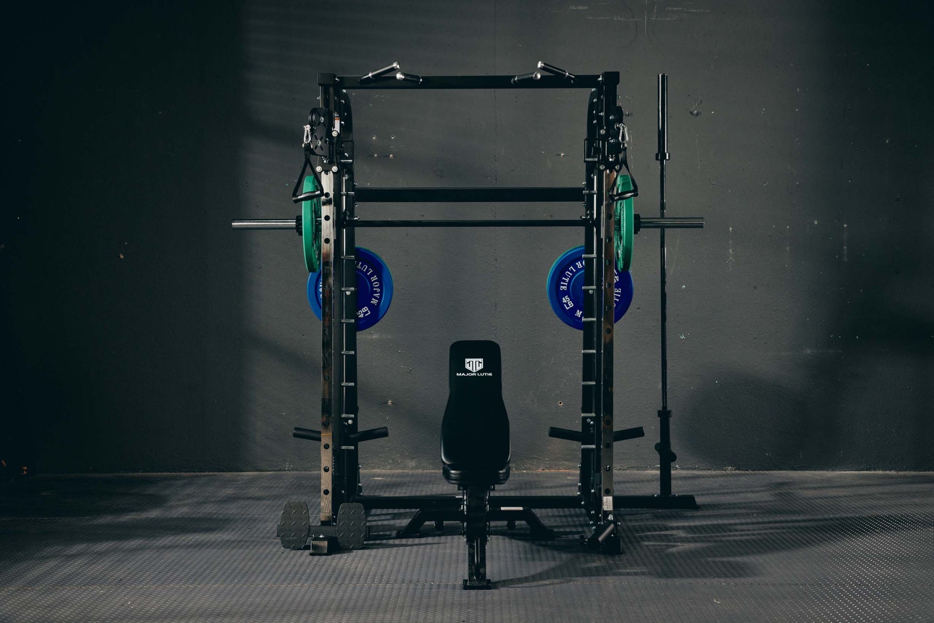 Multifunctional Smith machine with green and blue weight plates and an adjustable bench in a home gym.