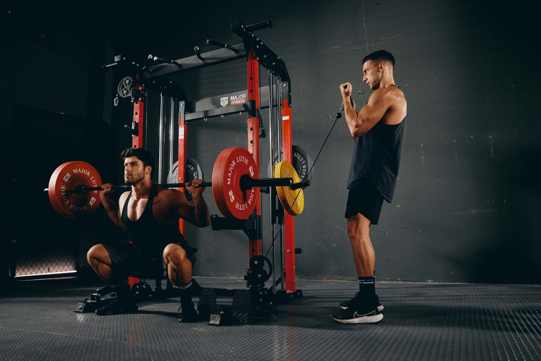 Men working out in a gym, one performing a barbell squat and the other doing cable curls.