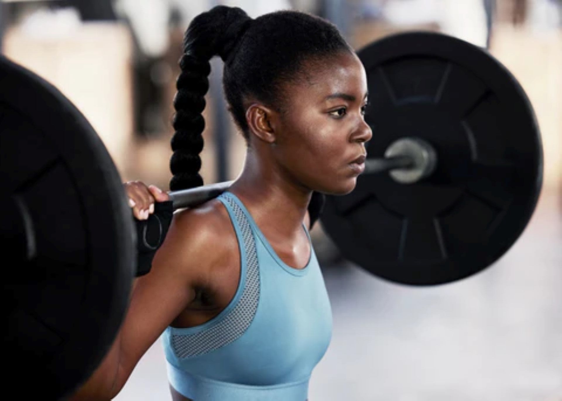 A woman working out by performing a barbell squat in a gym setting.