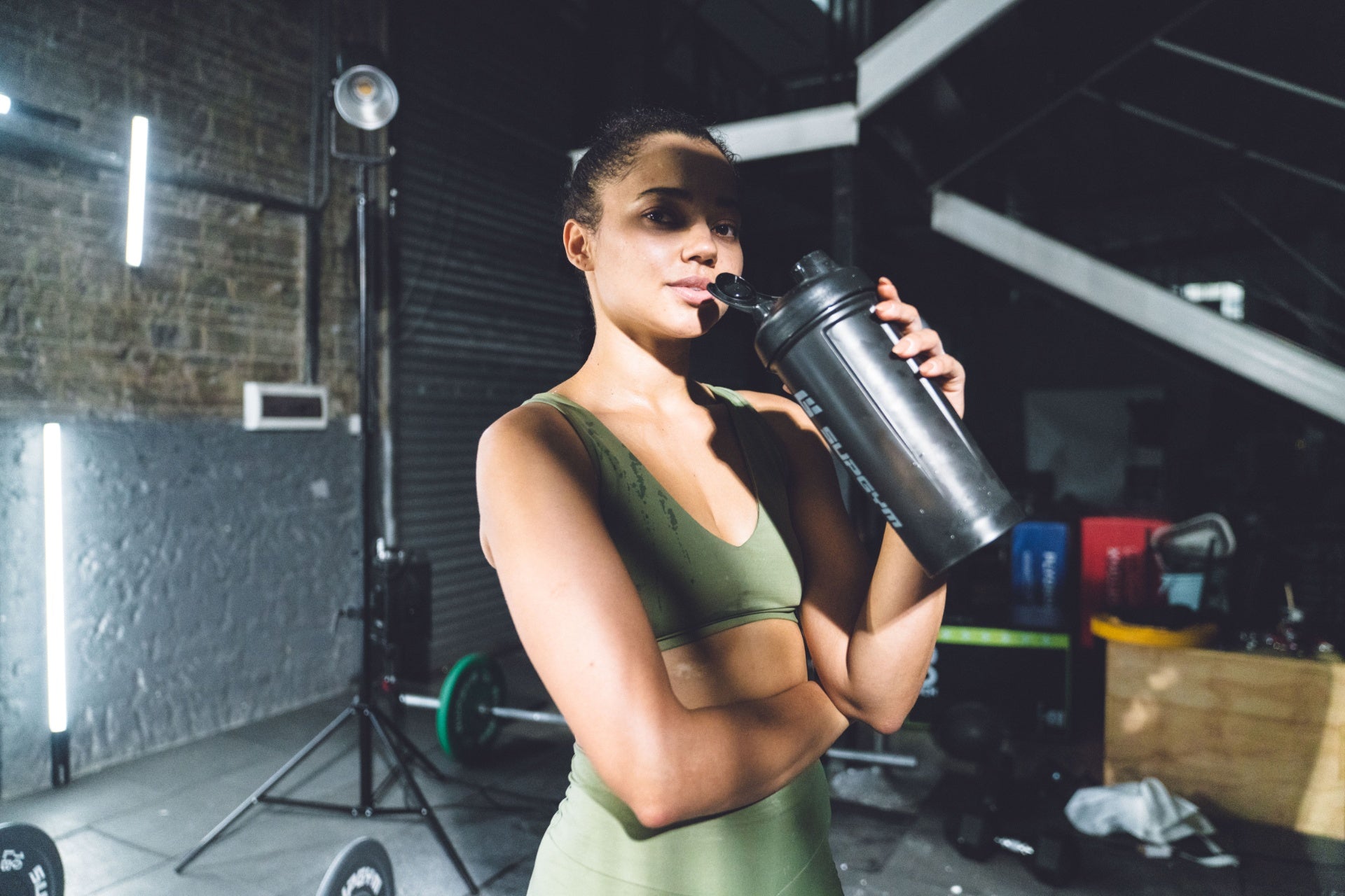 Woman drinking water from a shaker bottle during a workout in the gym.