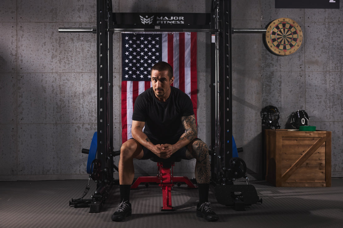 Athlete sitting on a bench resting between sets in a home gym setup with a smith machine.